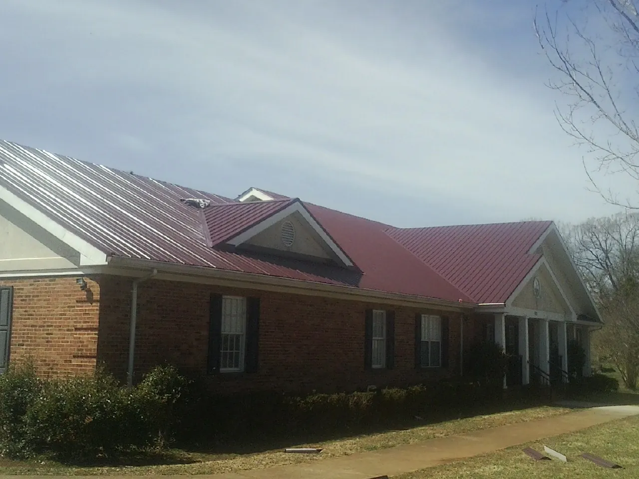 Red metal roof with gabled entries on a long brick building, from a Hail Damage Roof Repair job in Monticello