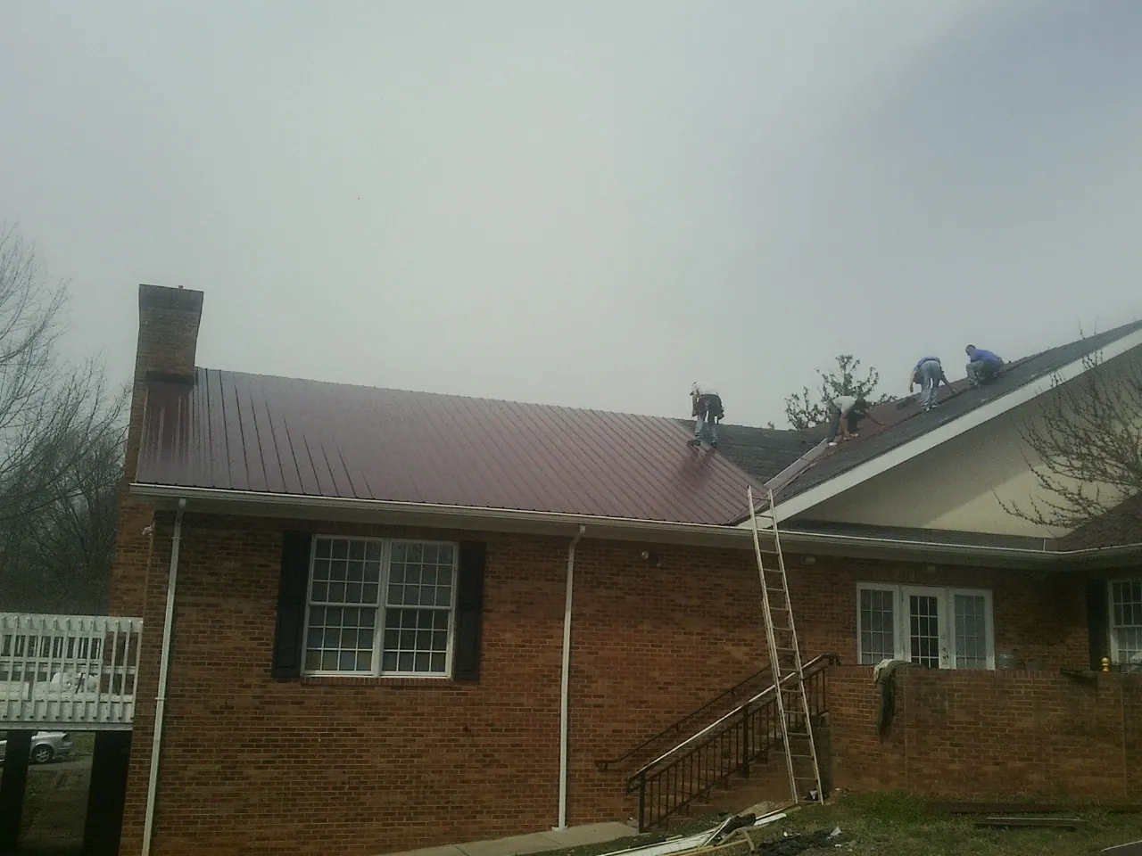 Crew setting red metal roofing panels on a brick home in Monticello