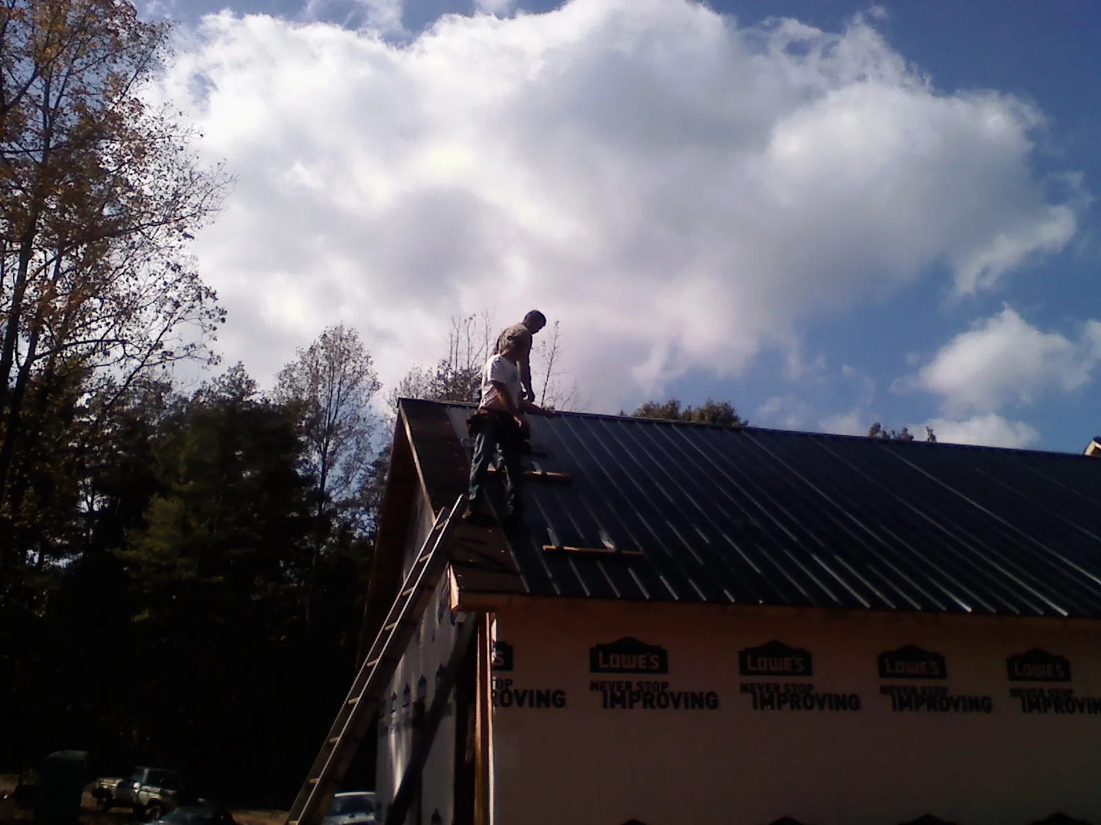 Roofer fastening dark metal panels high against a cloudy sky, from a Roof Inspection job in Monticello